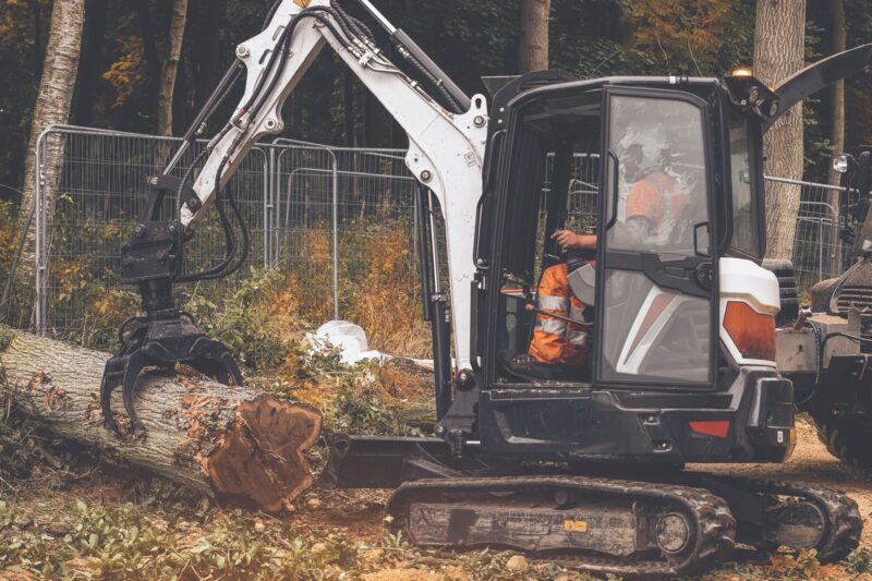 Excavator with a grapple lifting a felled tree in woodland